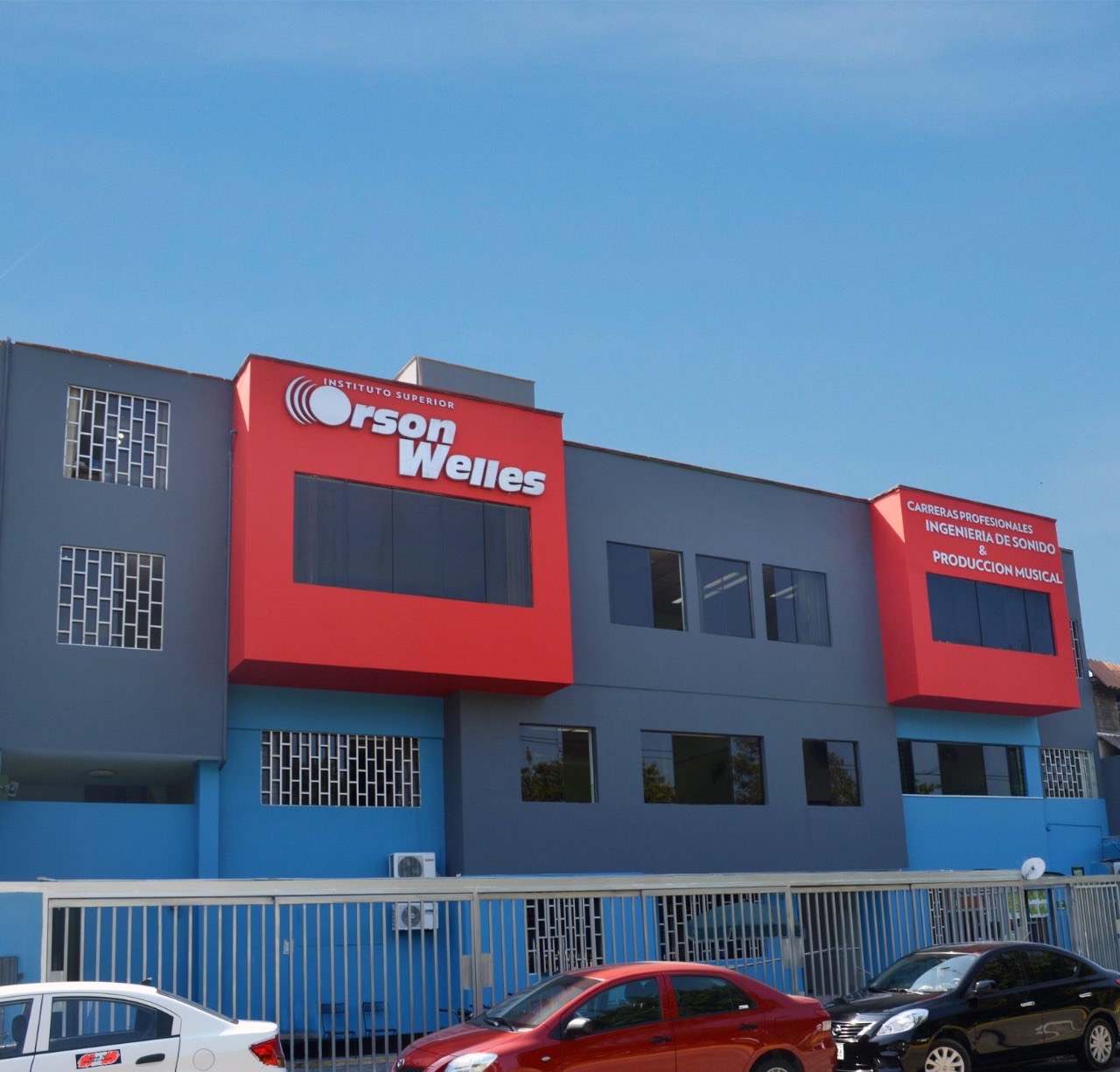 edificación de color gris azul y rojo se resalta en las secciónes de rojo los siguientes textos en el centro instituto superior Orson Welles a la derecha sobre otra sección en rojo está otro texto también en color blanco que dice Carreras profesionales ingeniería de sonido y producción musical