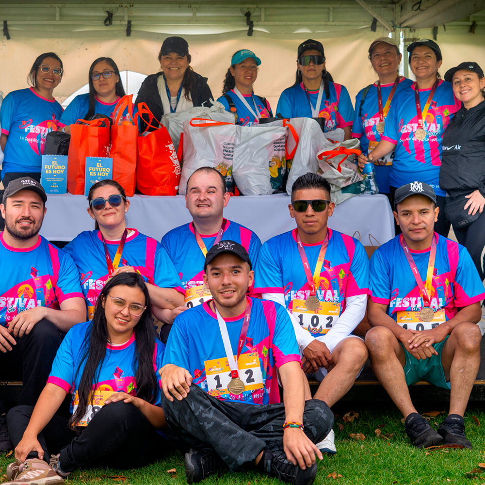 Andrea Carolina Chacón, junto a un grupo de participantes y colaboradores de la 5K Sin Límites posa frente a una mesa con las donaciones recibidas durante la jornada.