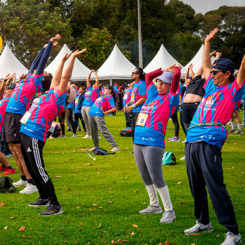Grupo de participantes realiza ejercicios de estiramiento con los brazos levantados durante el calentamiento previo a la carrera 5K Sin Límites, en el Parque de los Novios.
