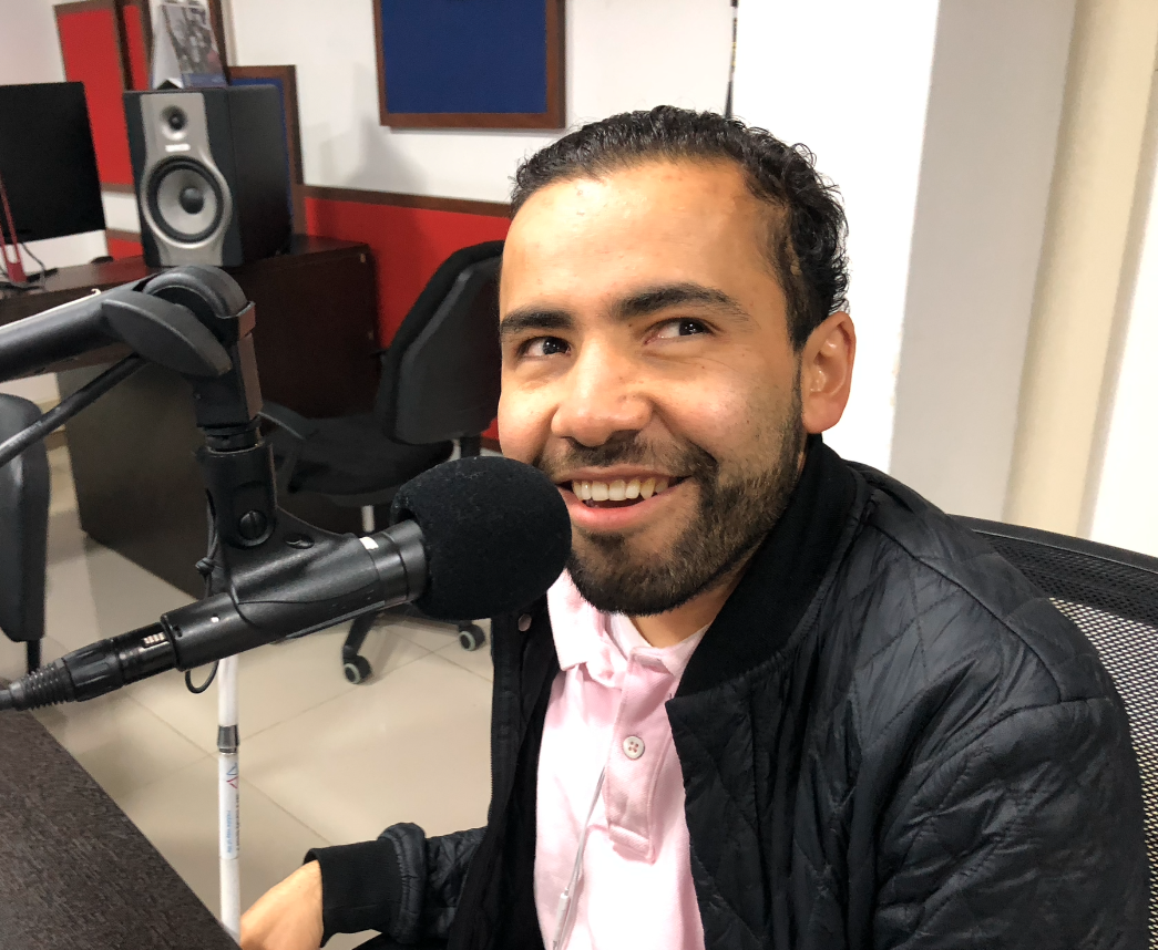 Imagen de carlos quintero, él sonríe, está en la cabina de INCIRadio, frente a él está un micrófono