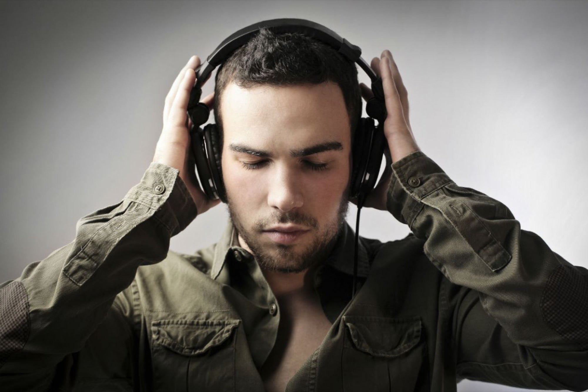 hombre con camisa verde, tiene sus ojos cerrados, con sus manos sostiene los auriculares que están en su cabeza