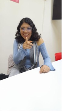Alessandra Baltazar participa en una conversación mientras señala al frente con uno de sus dedos, en un gesto que enfatiza una idea o comentario. La otra mano descansa sobre la mesa, acompañando naturalmente su intervención. La imagen captura un momento dinámico de interacción y comunicación.