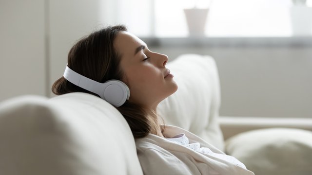 mujer vestida de blanco tiene los ojos cerrados usa unos audifónos de color blanco ella luce relajada