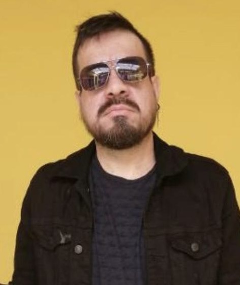 Braulio en primer plano el usa unos lentes oscuros, una chamara negra y un buzo de color azul oscuro 