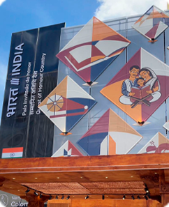 Fotografía de la Feria Internacional del Libro de Bogotá, del pabellón de la India como país invitado de honor, con ilustraciones geométricas de cometas de colores y una escena de dos personas leyendo.