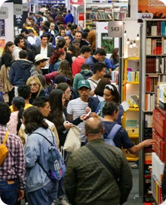 Visitantes recorriendo un pasillo lleno de stands y estanterías de libros durante la feria del Libro