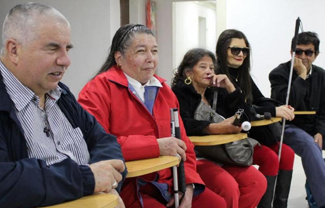 Grupo de 5 adultos con discapacidad visual, sentados en pupitres
