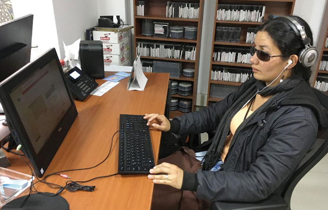 Mujer con discapacidad visual, trabajando en un computador de escritorio, usando el teclado para interactuar con el computador