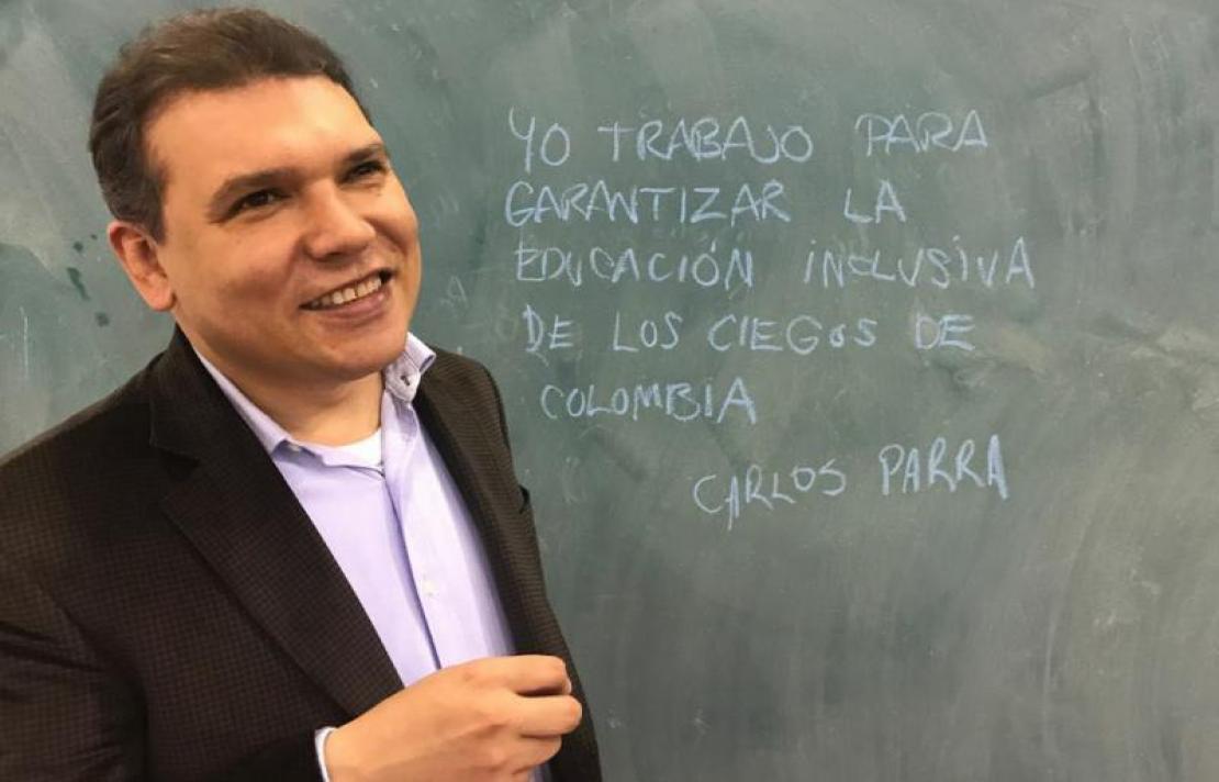 Carlos Parra Dussan, Director General Instituto Nacional para Ciegos - INCI, en un tablero fondo berde con el texto " Yo trabajo para garantizar la educación inclusiva de los ciegos de Colombia"