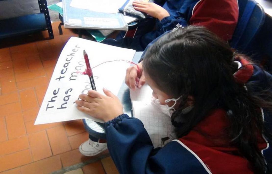 Niña con baja visión escribiendo sus notas de inglés en una hoja tamaño carta