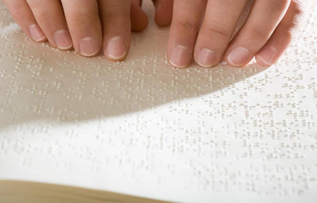 Cartilla en braille de EPS Foto, una cartilla en braille con dos manos pasando sobre los caracteres