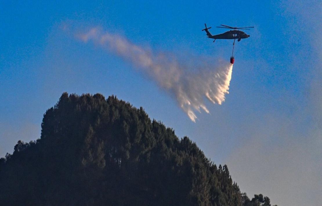 un helicoptero esparce agua en la montaña que está incendiado