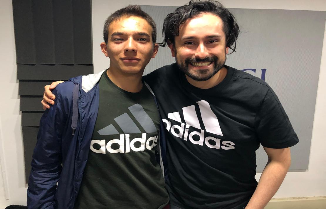 Camilo Garnica y Henry Díaz sonríen, están en la cabina de INCIRadio, ellos visten la misma camiseta que tiene el lago de Adidas