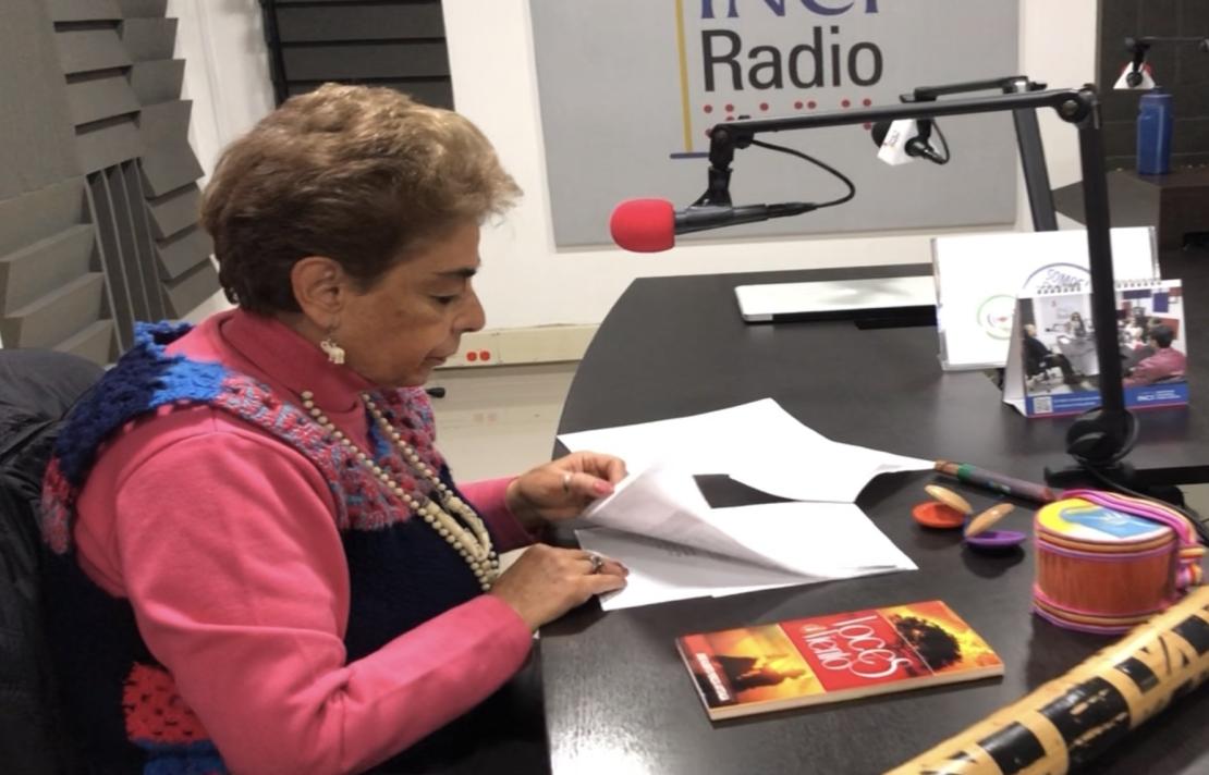 cabina de inciradio, edda está de medio lado frente al microfono, sobre la mesa está el libreto libros e instrumentos musicales