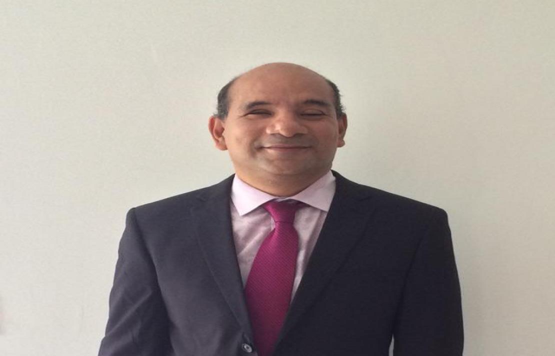 Imagen de Demetrio Shend, el sonríe, viste un traje de color gris oscuro, camisa rosada y corbata rosada