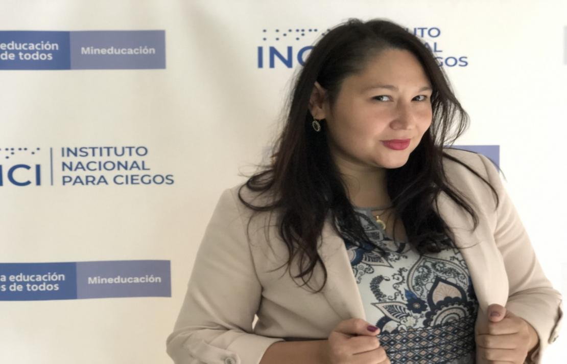 imagen de leidy hoyos ella está frente a un pendón del INCI, ella viste un blazer color marfiil