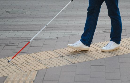 Fotografía - Peatón caminando con bastón sobre baldosas podo táctiles con