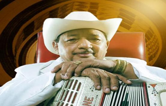 frente a un fondo animado de un sombrero vueltiao y vistiendo un traje y sombrero blanco está lisandro mesa quien posa sus manos sobre un acordeón