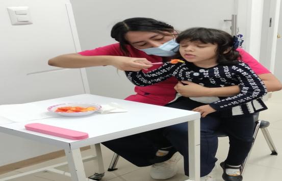 Azmin Zuñiga da de comer a una niña que reposa en sus piernas