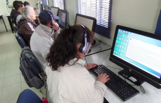 Grupo de personas trabajando en una sala de computo, en el primer plano se ve una mujer escribiendo por medio del teclado