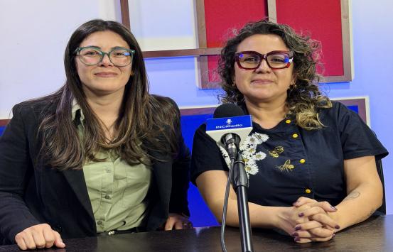 A la izquierda de la foto está  Andrea Carolina Chacón Castillo, directora general del Instituto Nacional para Ciegos – INCI. Ella viste un saco oscuro sobre una blusa verde clara y transmite serenidad y profesionalismo. Y A la derecha se encuentra Adriana Ángel Forero, directora de la Feria Internacional del Libro de Bogotá – FILBo. Ella lleva una blusa oscura con bordados de abejas y flores, que le dan un toque distintivo y elegante. El fondo está compuesto por paneles geométricos en tonos rojo, azul y bl