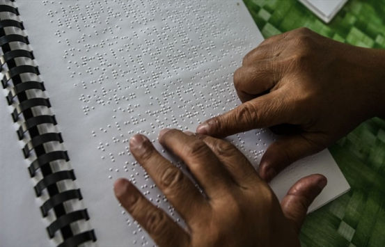 Manos de un hombre leyendo un libro en Braille